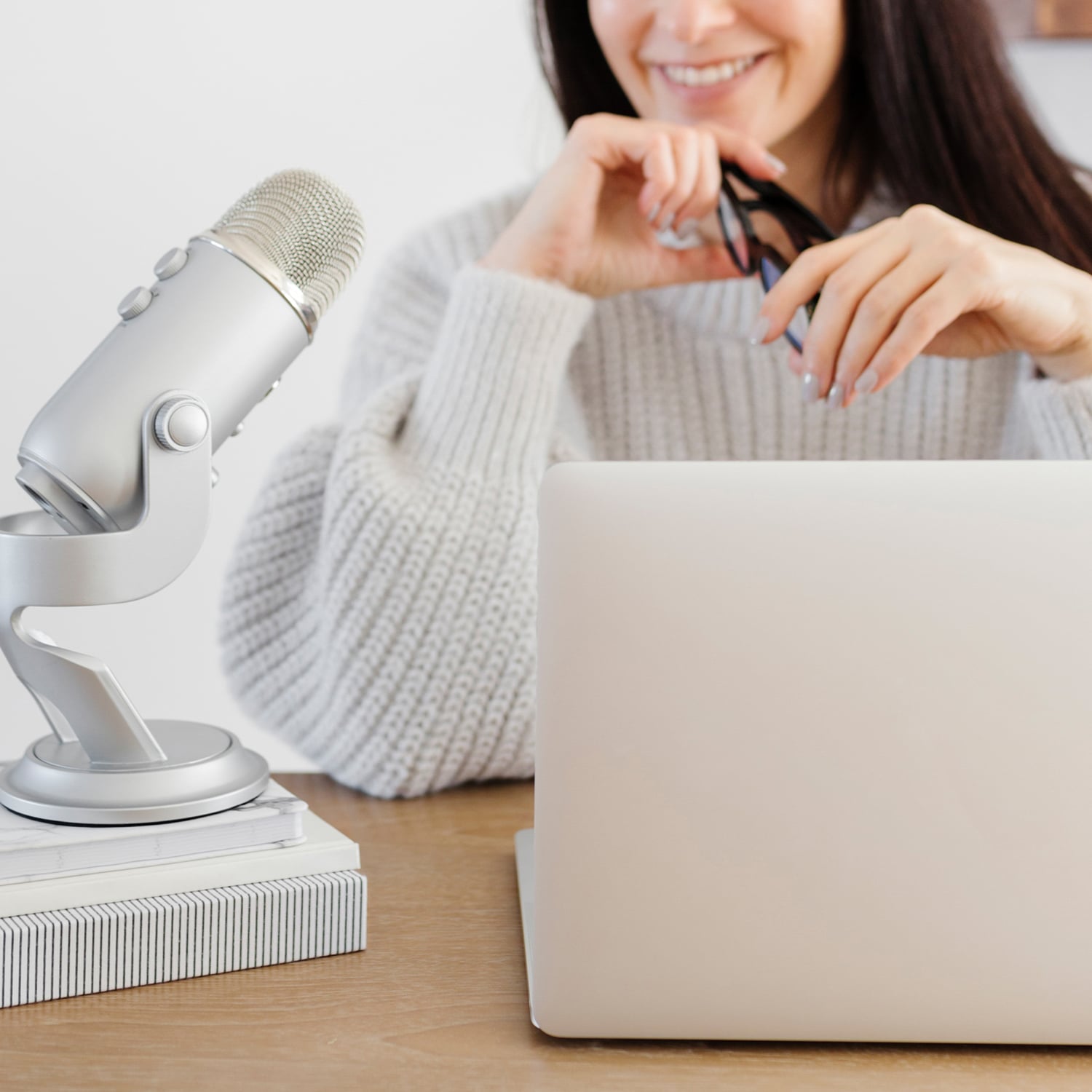 An open laptop and microphone on a desk in front of a woman in the background with long dark hair